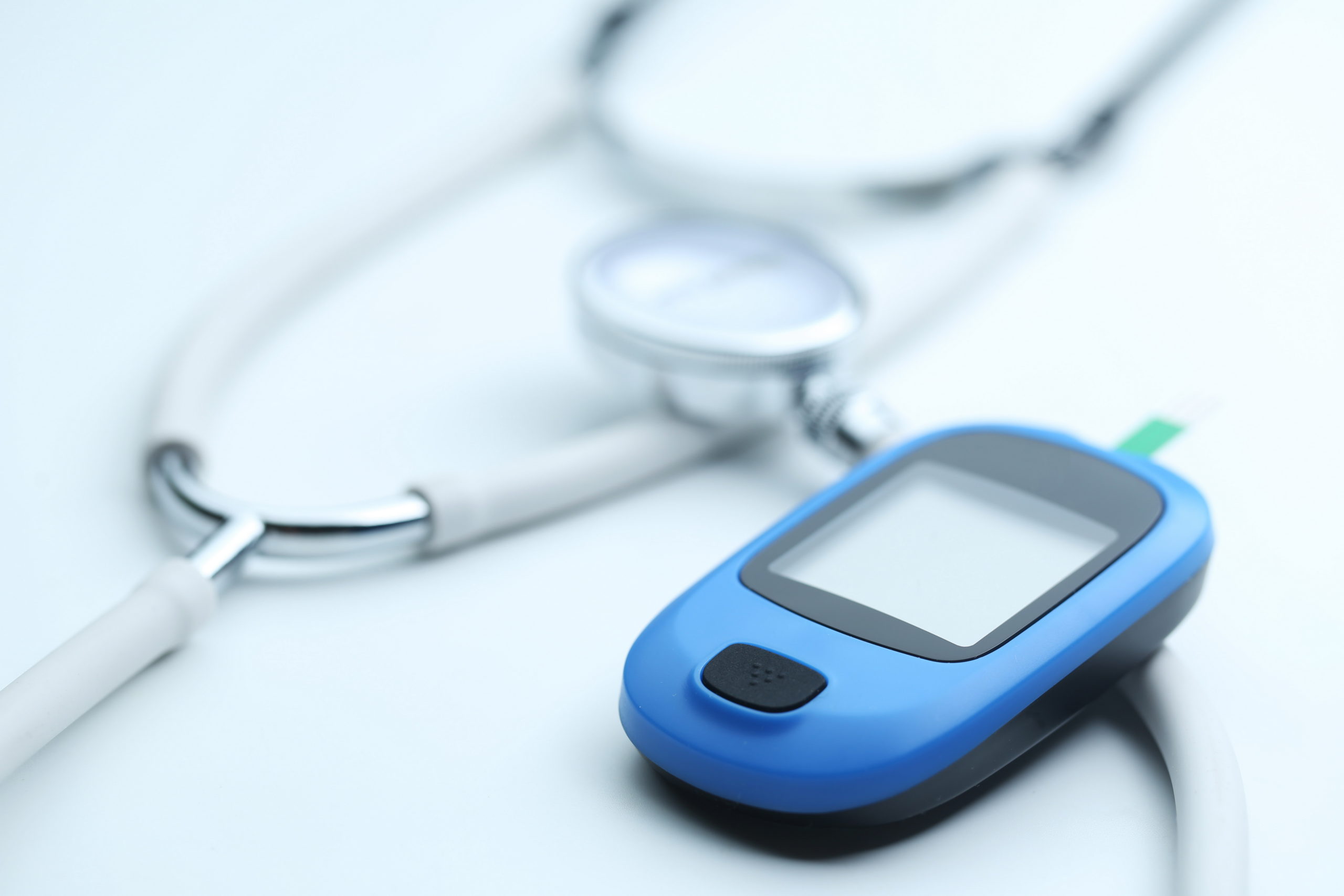 Blood glucose meter and stethoscope on white background