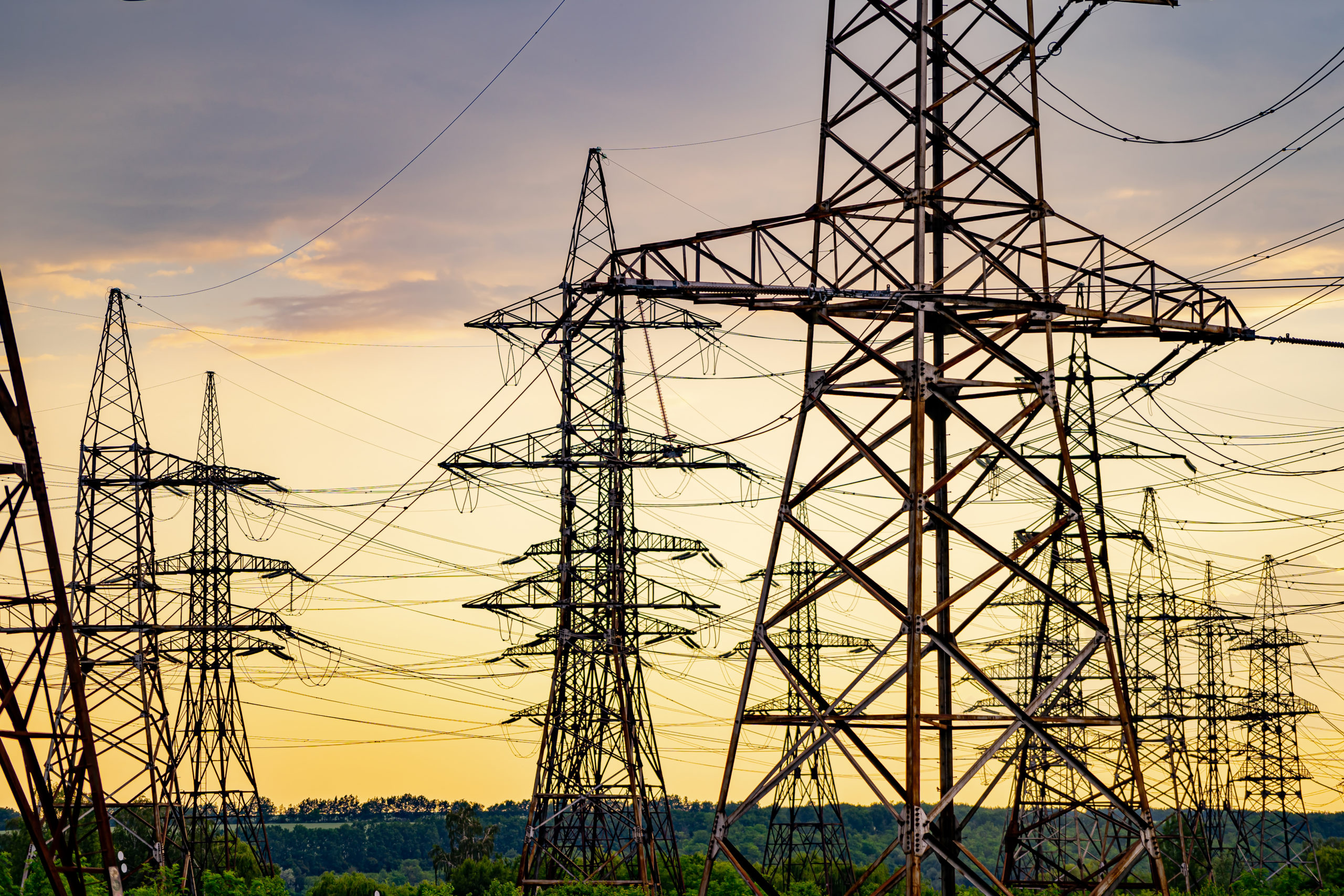 Electricity pylons bearing the power supply across a rural landscape during sunset. Selective focus.